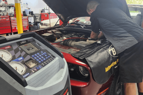 Is it time for a car ac recharge in Chandler AZ? Image of Mac's Auto Repair technician using an ac compressor testing machine on a red dodge challenger that is in the shop.
