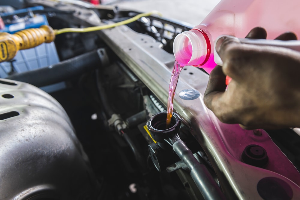 Coolant System Flush Service in Chandler, AZ at Mac’s Complete Auto Repair. Image of an auto mechanic pouring coolant fluid into the car radiator fill hole during the service.