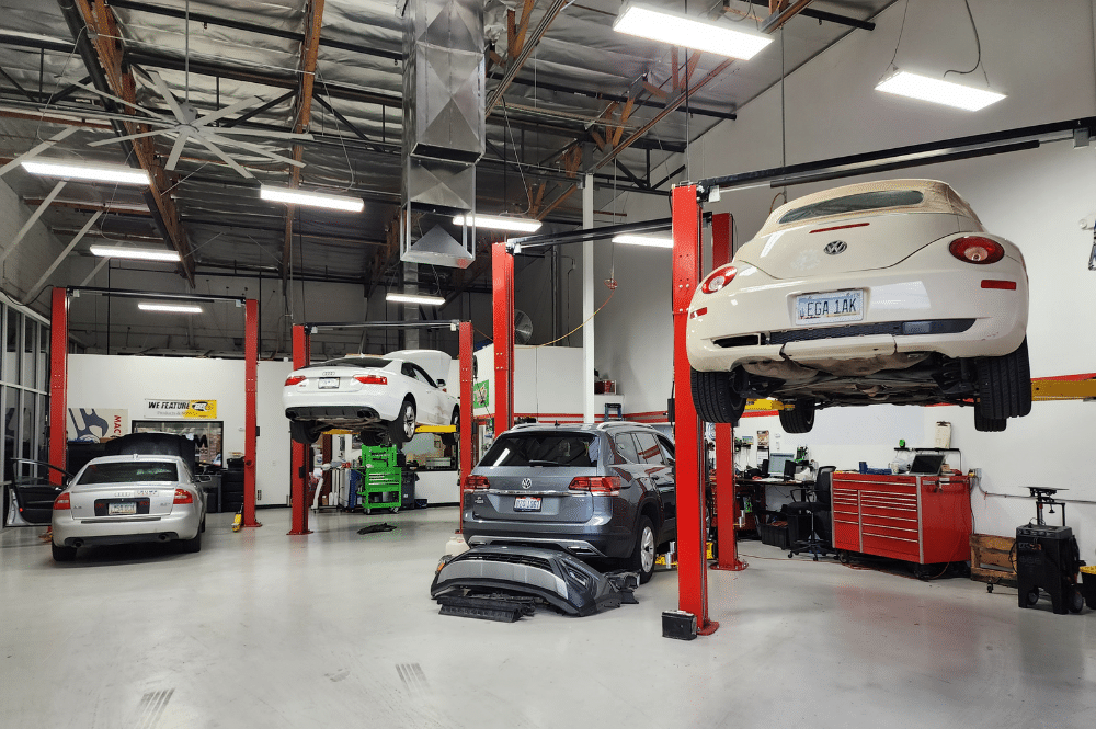 Auto repair in Chandler, AZ at Mac’s Complete Auto Repair. Image of the garage featuring four cars: an Audi and a Volkswagen on lifts, a Volkswagen undergoing wheel alignment, and another Audi having AC repair.