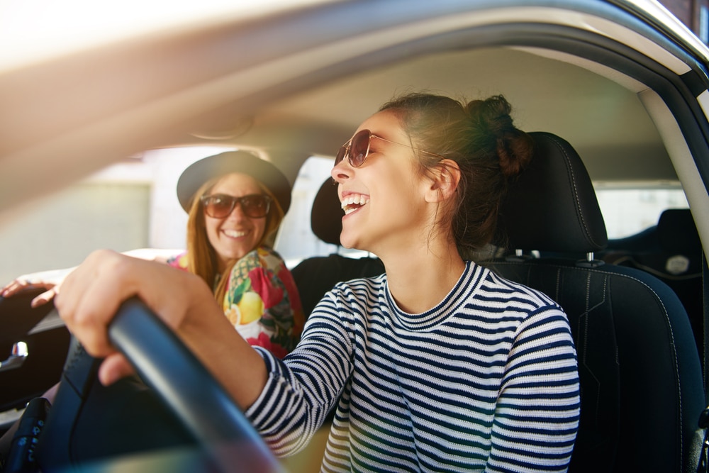 How to Prepare Your Volkswagen for a Summer Adventure by Mac’s Complete Auto Repair. Two women in a Volkswagen, smiling and ready for a summer road trip, symbolizing the importance of preparing your car for a safe and enjoyable journey.