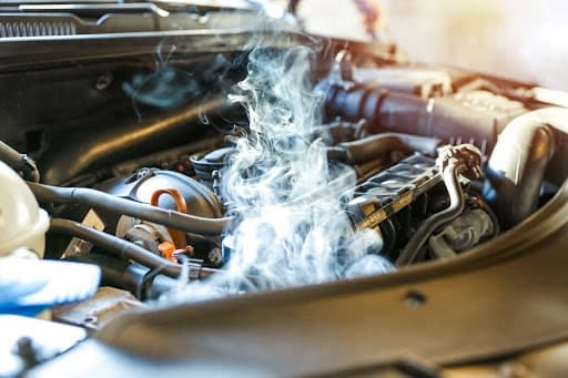 Fall vehicle maintenance tips in Chandler, AZ to prevent engine overheating and ensure cooling system efficiency with Mac's Complete Auto Repair. Image of smoke around radiator of a car engine with hood up due to overheating.