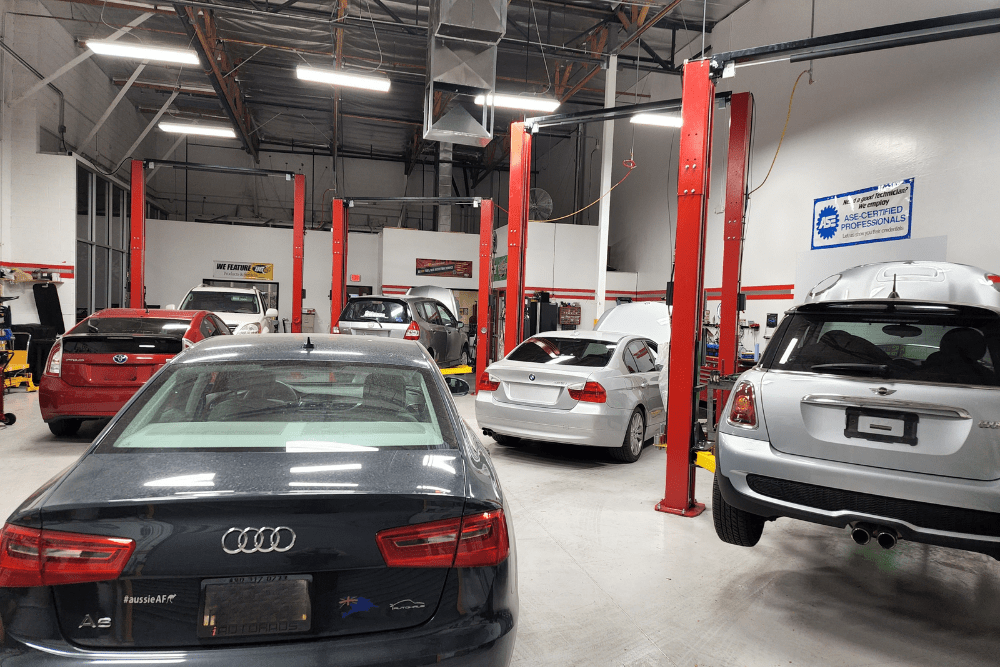 European and domestic vehicles inside a clean, well-lit Mac’s Complete Auto Repair in Chandler, AZ, with multiple service bays and red hydraulic lifts.