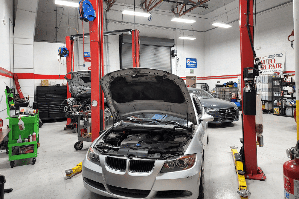 BMW and Audi vehicles undergoing service in Mac’s Complete Auto Repair shop, with open hoods, red hydraulic lifts, and tools organized for auto repair near you.