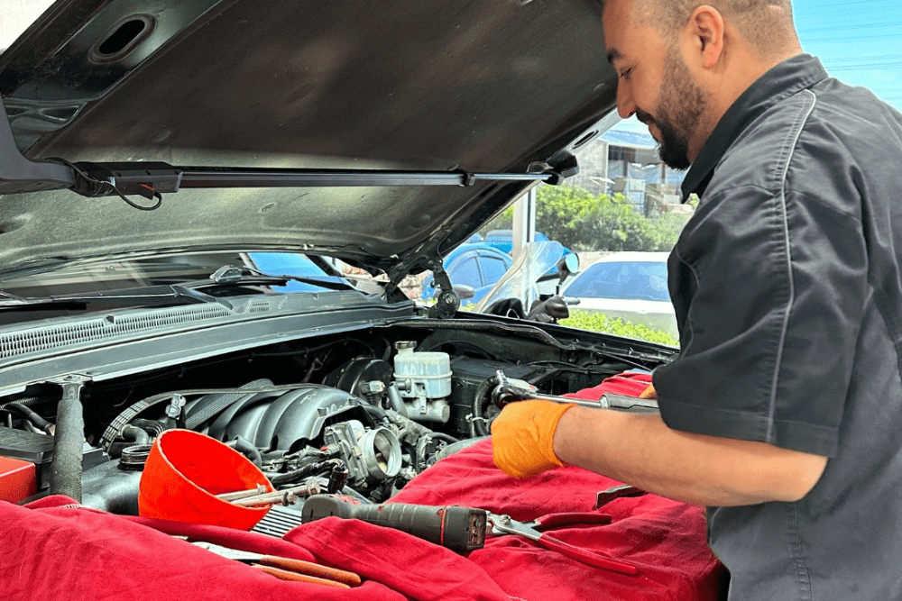 Auto repair in Gilbert, AZ by Mac's Complete Auto Repair. Technician performs summer vehicle maintenance with the hood open, ensuring proper cooling for hot weather driving.